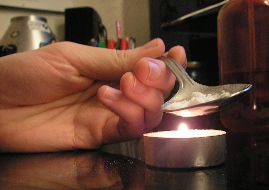 A hand holding a spoon of white powder over a candle flame